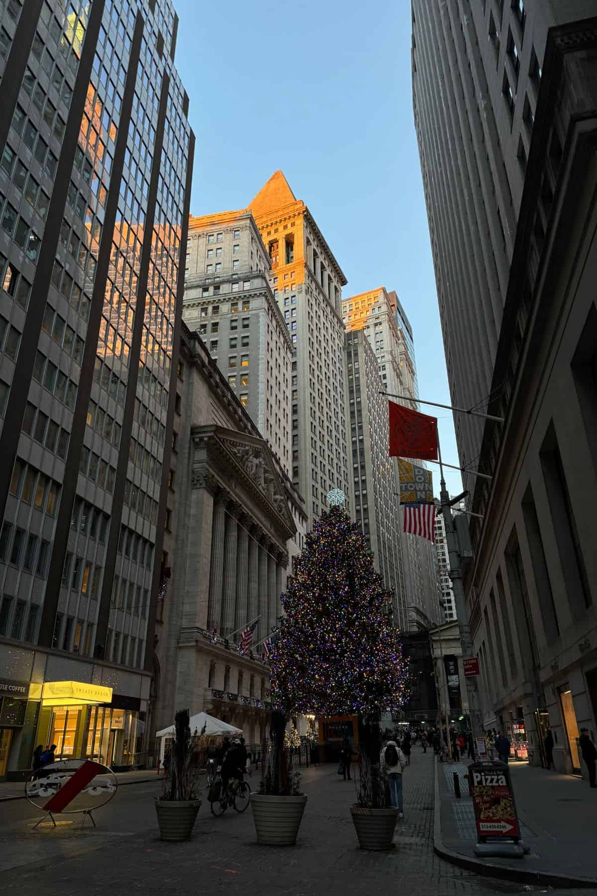 A decorated Christmas tree stands in front of tall office buildings on a city street, with people walking around and American flags displayed—an iconic scene perfect for your One Day in NYC Itinerary.