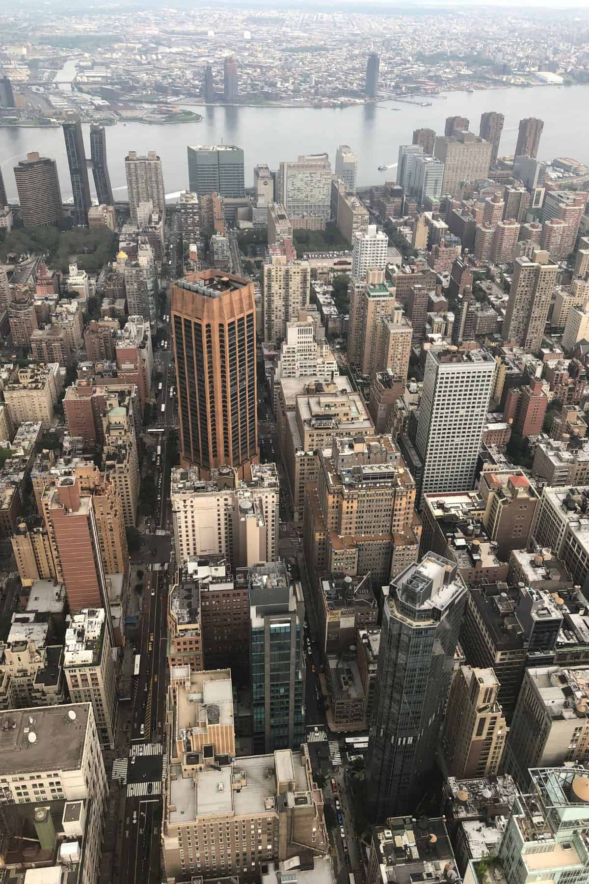 Aerial view of densely packed tall buildings in Manhattan, New York City—an iconic sight often seen on a One Day in NYC Itinerary—with the East River and more skyscrapers stretching into the background.