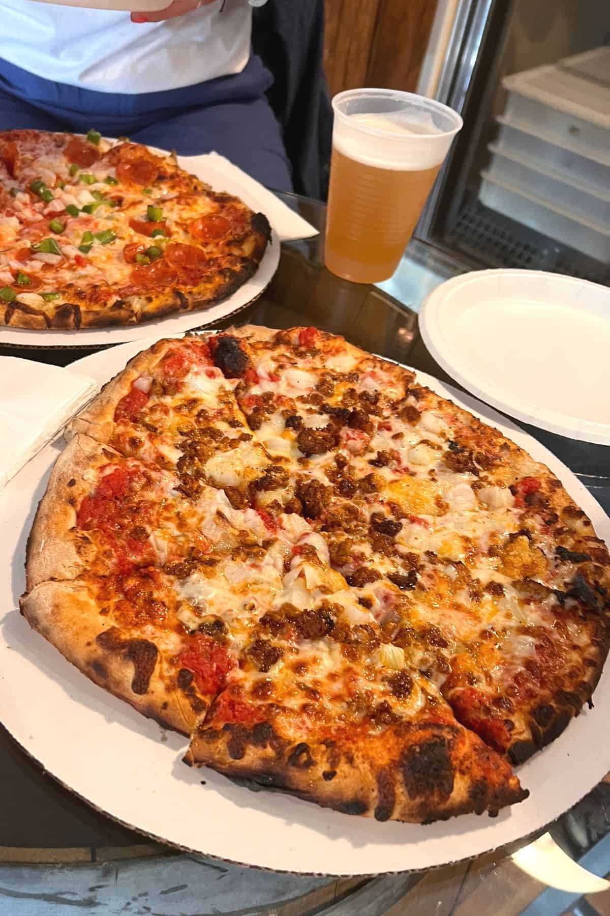 two pizzas with tap beer on table.