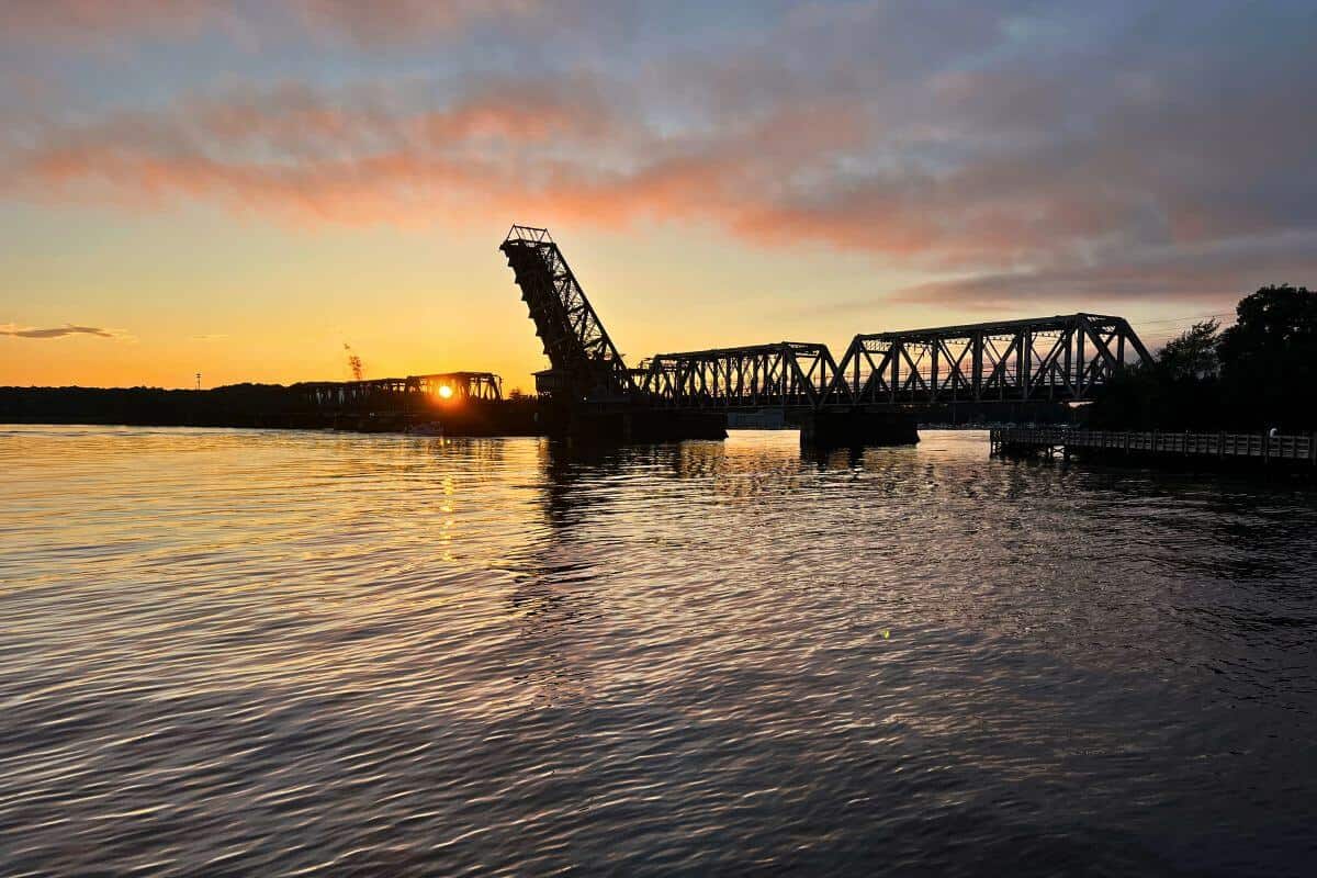 A train bridge over a body of water at sunset.