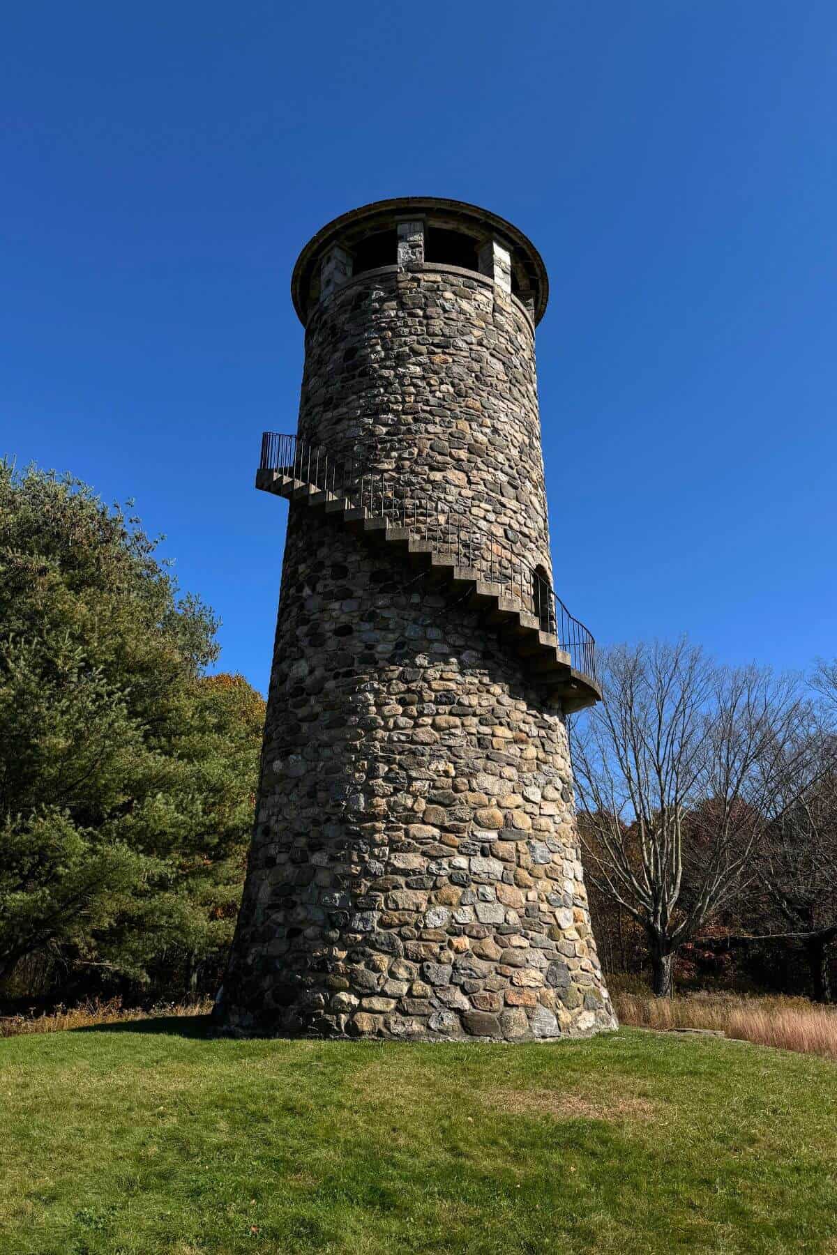 A stone tower in the middle of a grassy field.