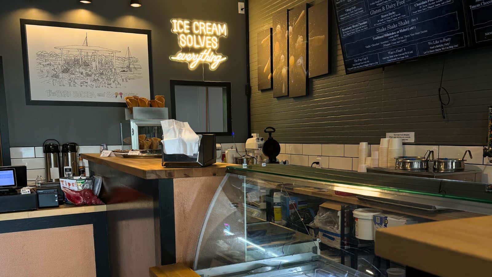 Ice cream shop interior with a sign reading "Ice Cream Solves Everything," a counter with supplies, and menu boards on the wall.