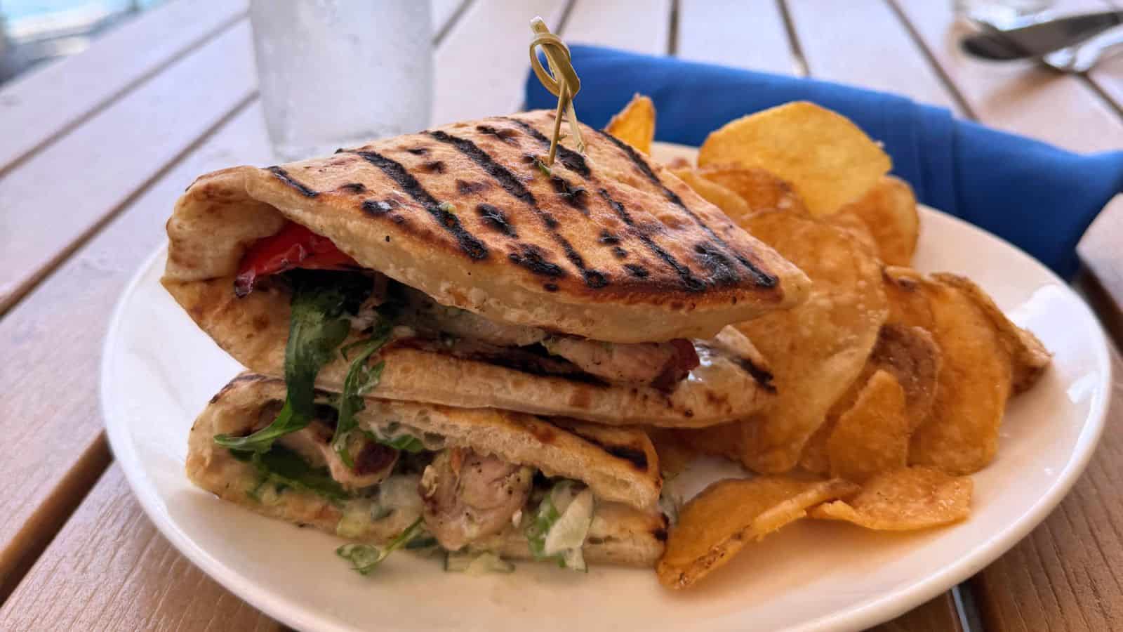 Grilled flatbread sandwich with lettuce, grilled chicken, and tomato, served with a side of potato chips on a white plate—fuel up before exploring things to do in Stonington Connecticut.
