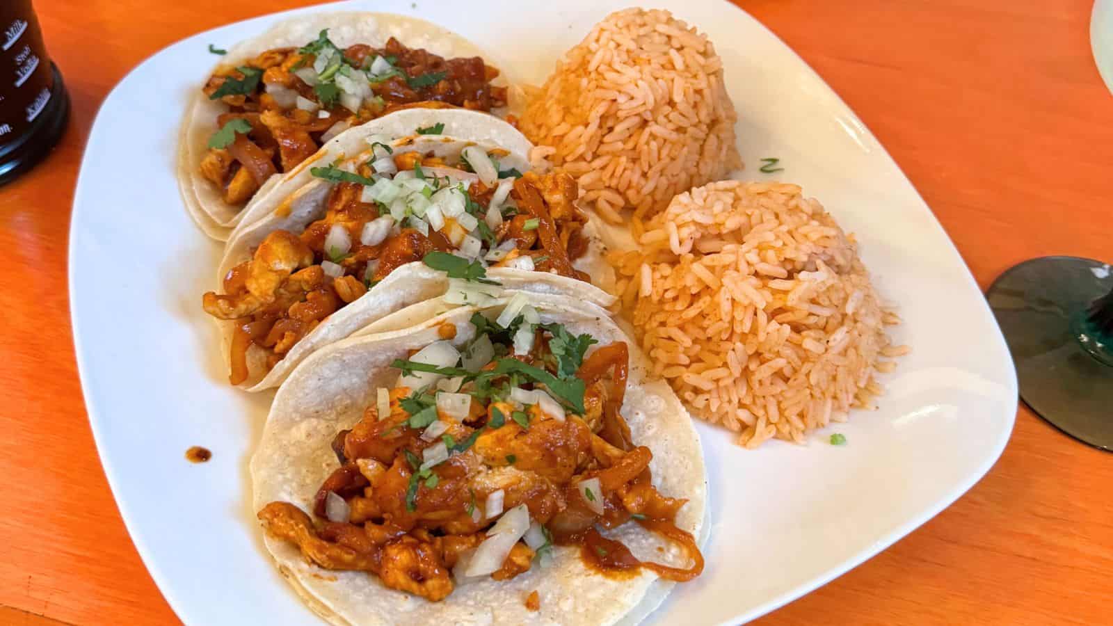 Three chicken tacos topped with onions and cilantro, served with two portions of Mexican rice on a white plate—a delicious highlight among the things to do in Stonington Connecticut.