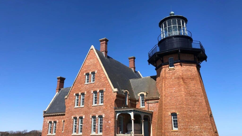 A red brick lighthouse with a sloped roof stands under a clear blue sky.