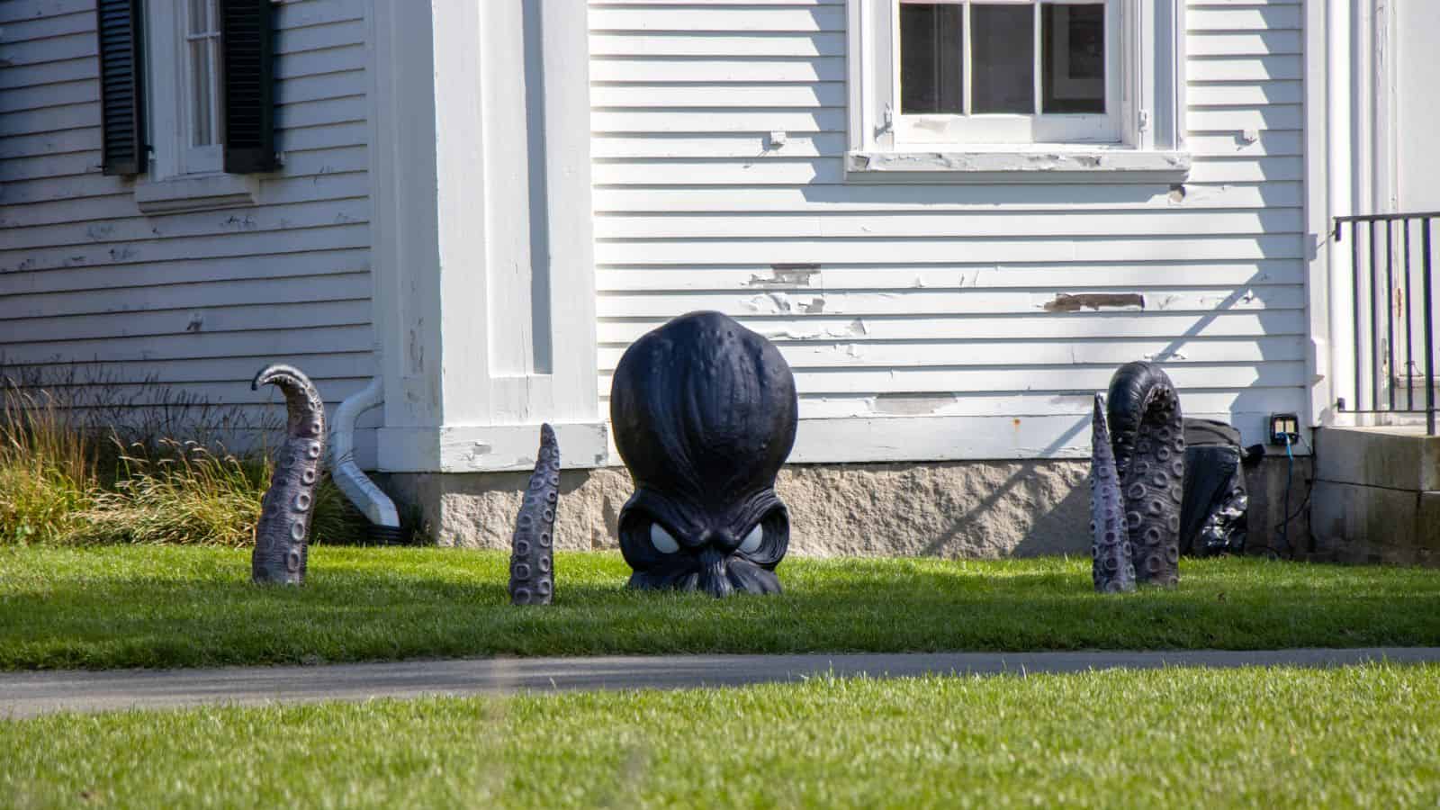 Menacing octopus tentacle sculptures in front of a white house, creating a spooky outdoor decor scene for Halloween or outdoor art.