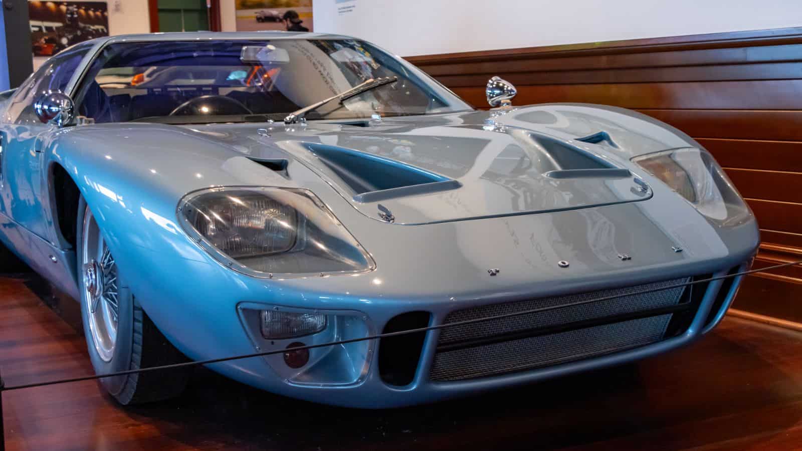 A light blue vintage sports car is displayed indoors on a polished wooden floor with a barrier in front, reminiscent of classic auto showcases in Newport, Rhode Island.