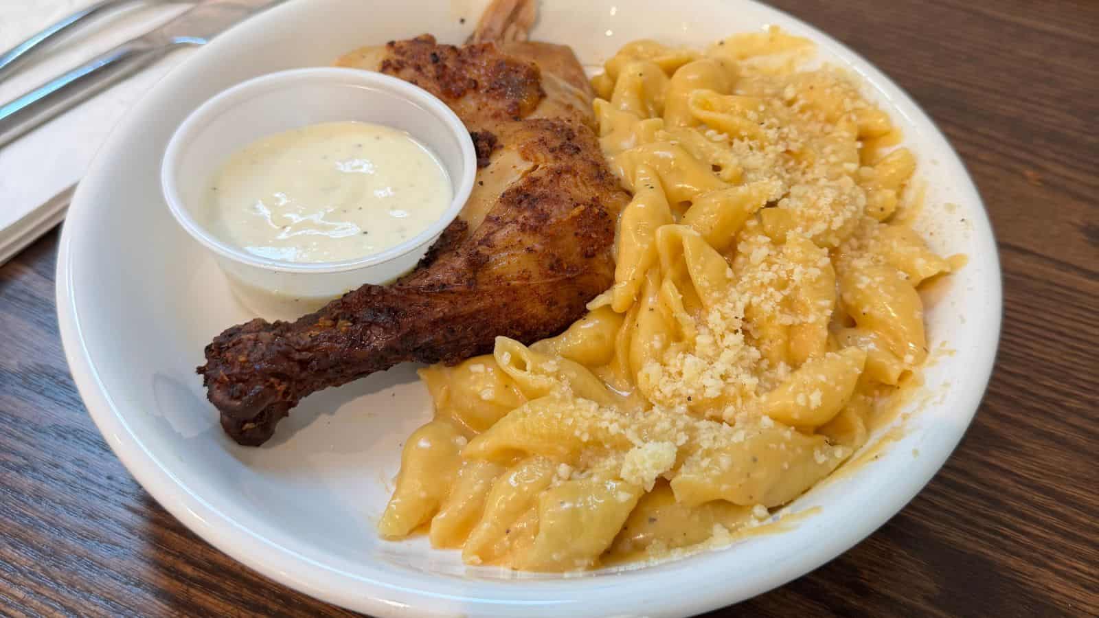 A plate with baked chicken, macaroni and cheese topped with grated cheese, and a small cup of white dipping sauce—perfect comfort food after exploring things to do in Old Saybrook.