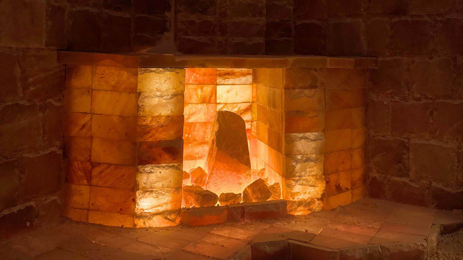 A fireplace constructed from illuminated salt blocks, emitting a warm orange and yellow glow, set against a background of stone or salt bricks—one of the unique things to do in Niantic CT.