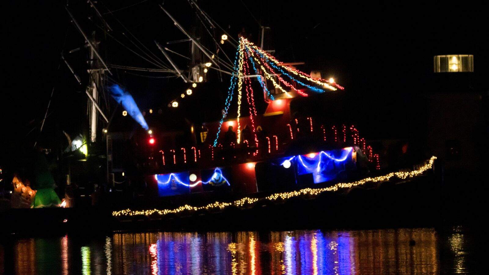 A boat decorated with colorful string lights is docked at night, its lights reflecting on the water—one of the festive things to do in Connecticut this holiday season.