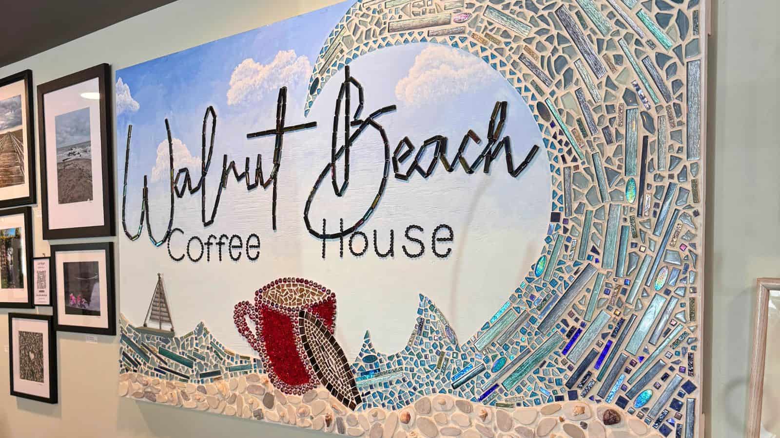 Mosaic wall art at Walnut Beach Coffee House, one of the standout Connecticut coffee shops, features a stylized wave, a red coffee cup, and the café's name in large script. Framed photos are displayed on the adjacent wall.