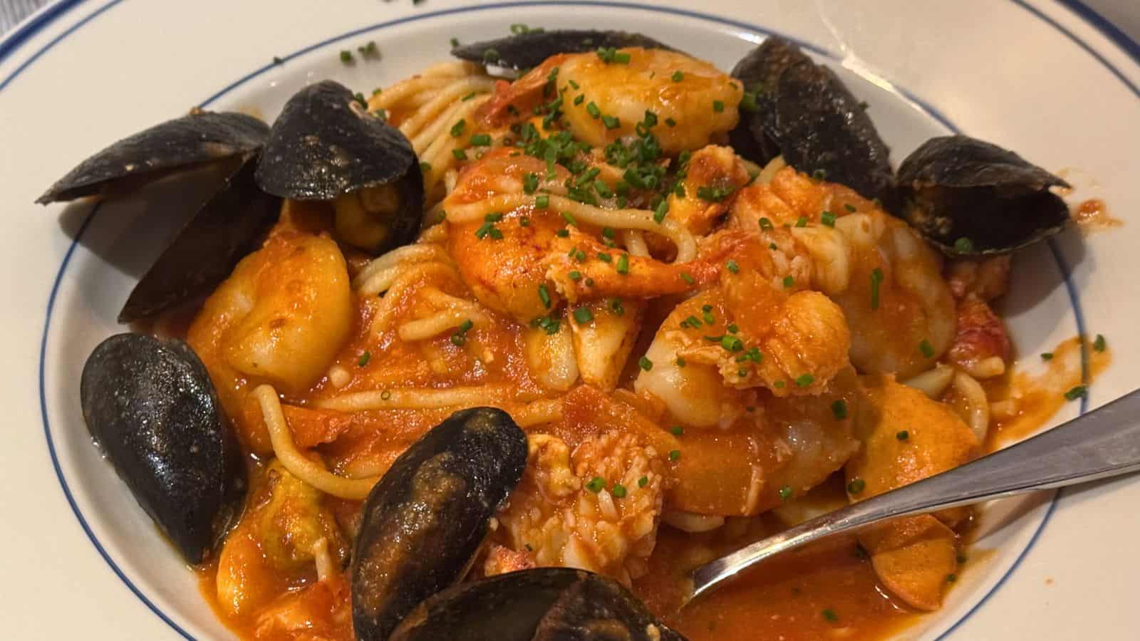 A plate of seafood pasta with mussels, shrimp, and gnocchi in a tomato-based sauce, garnished with chopped chives and served with a fork—a classic taste of Mystic CT’s coastal flavors.