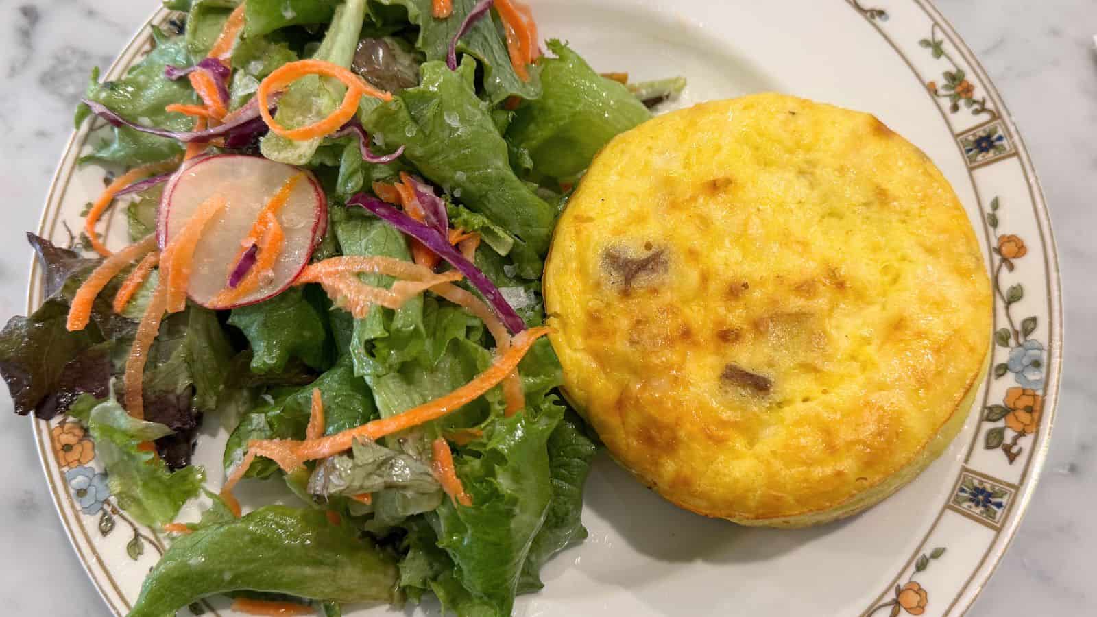 A plate with a mixed green salad featuring carrots and radishes sits next to a round, baked egg dish—possibly a quiche or frittata—offering a fresh taste you might enjoy in Norwich, Connecticut.