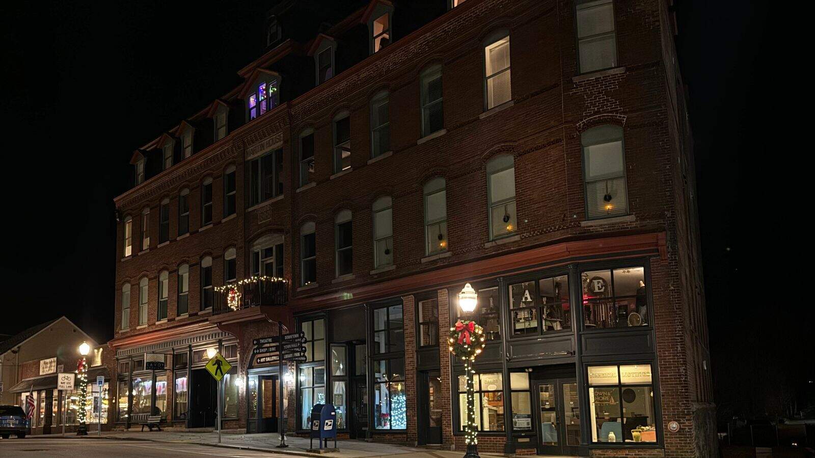 A three-story brick building in Westerly, Rhode Island, with shops on the ground floor and lit windows at night; street lamps and holiday decorations are visible.