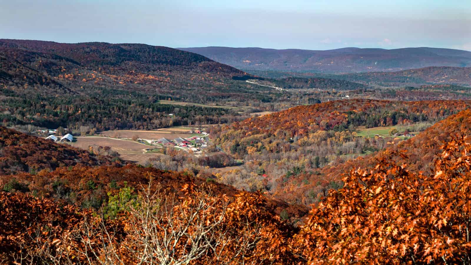 A panoramic view of a rural valley with scattered farms, surrounded by rolling hills covered in autumn foliage.