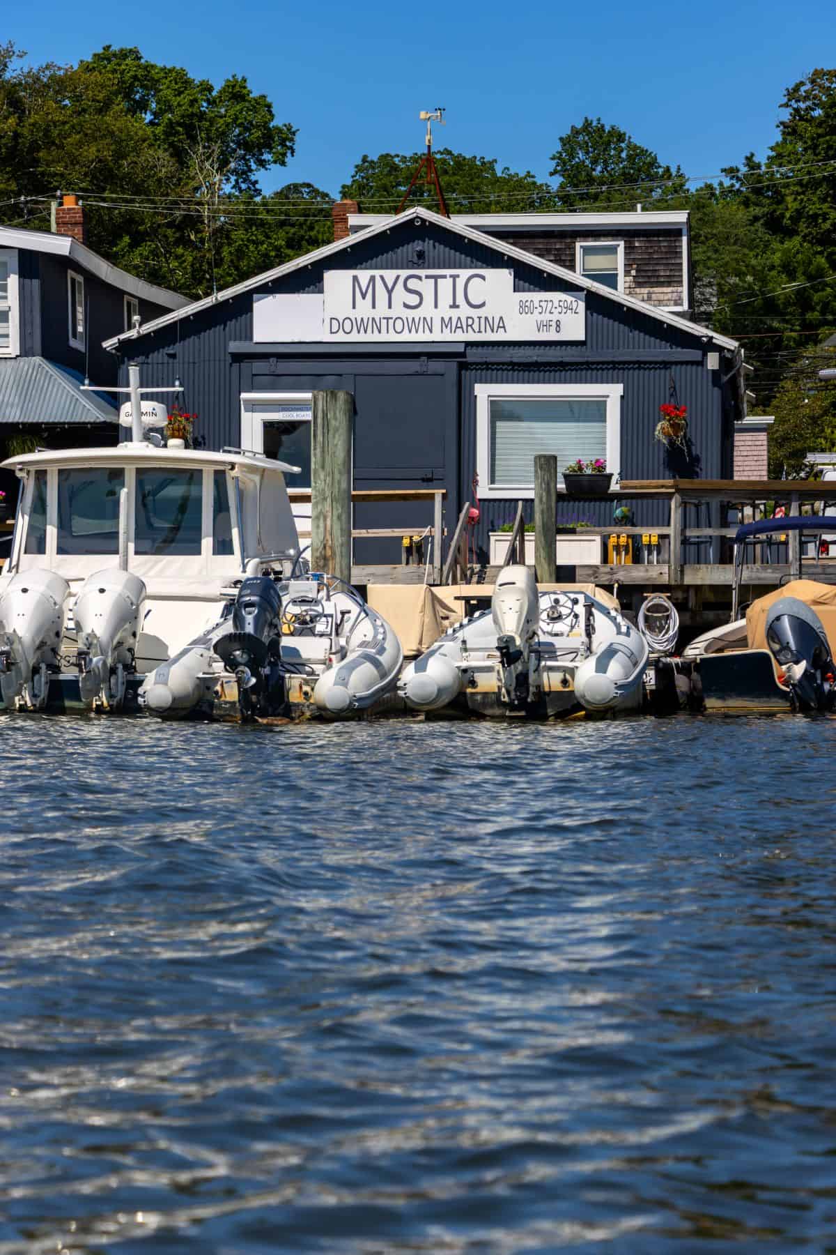 A marina with several docked boats in front of a building labeled "Mystic Downtown Marina" on a sunny day.