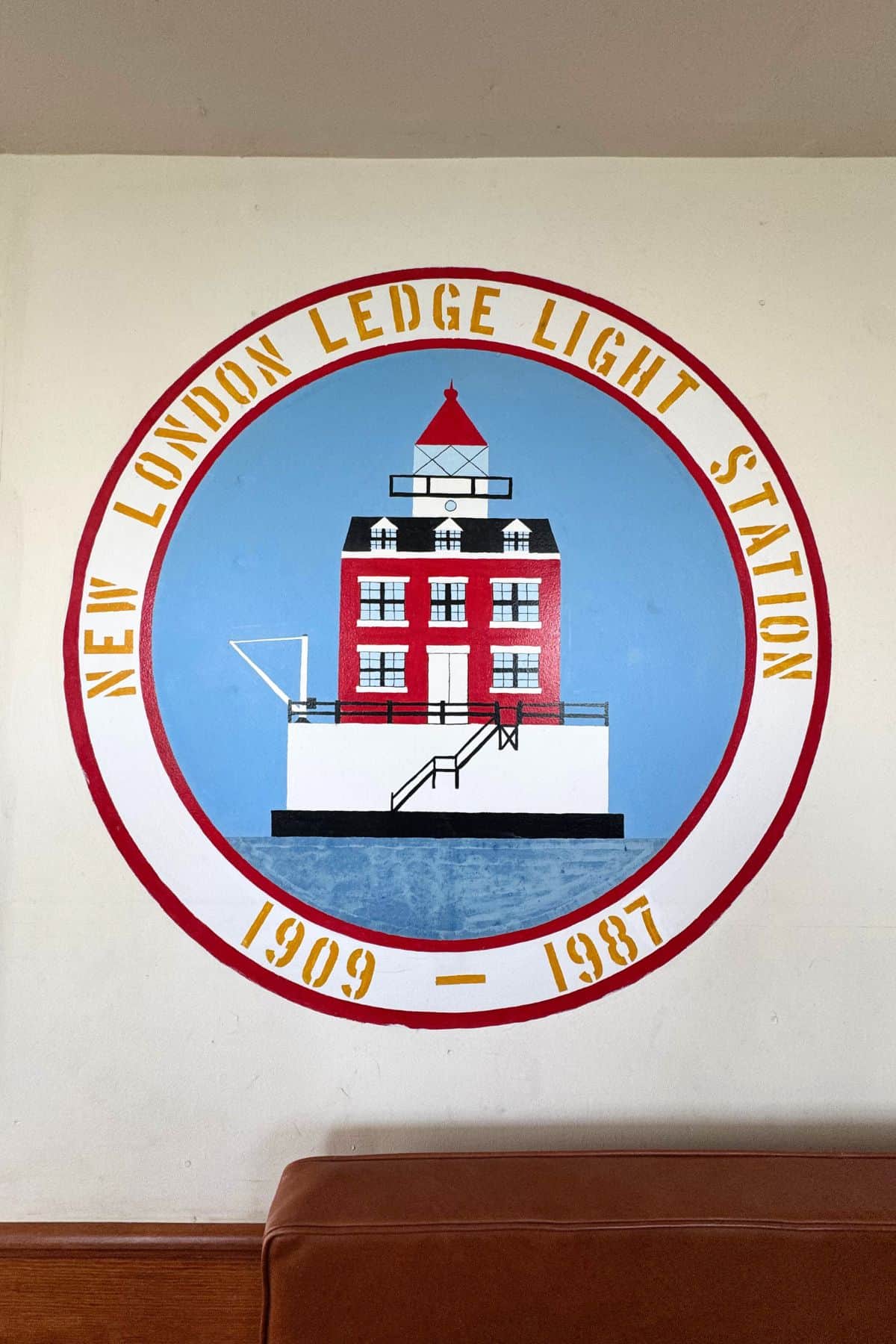 A circular mural shows the New London Ledge Light Station, featuring a red and white lighthouse with the years 1909–1987 and the station name around the border.