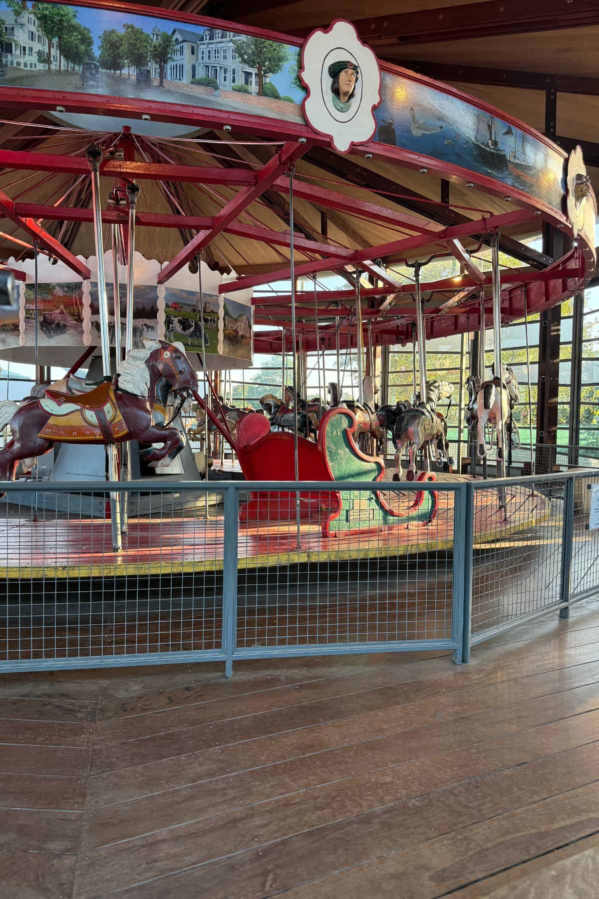 A vintage carousel with painted horses and a chariot stands inside a pavilion, surrounded by metal railings.