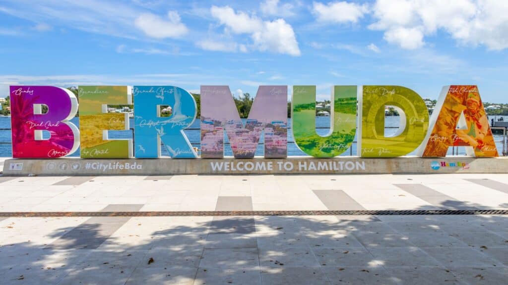Large colorful letters spelling "BERMUDA" with "WELCOME TO HAMILTON" below, set outdoors under a blue sky with trees and buildings in the background.