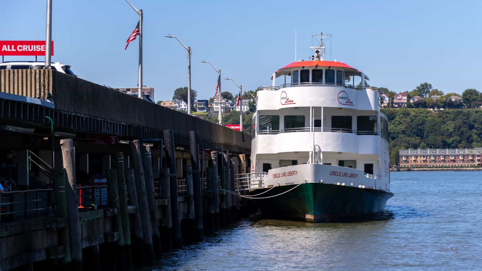 A white passenger ferry named "Circle Line XVII" is docked at a pier on a sunny day, with buildings and trees visible in the background.