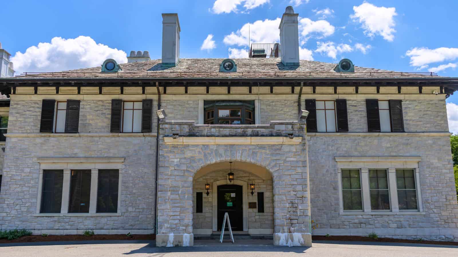 A large stone building with black shutters, multiple chimneys, and an arched entrance under a partly cloudy sky.