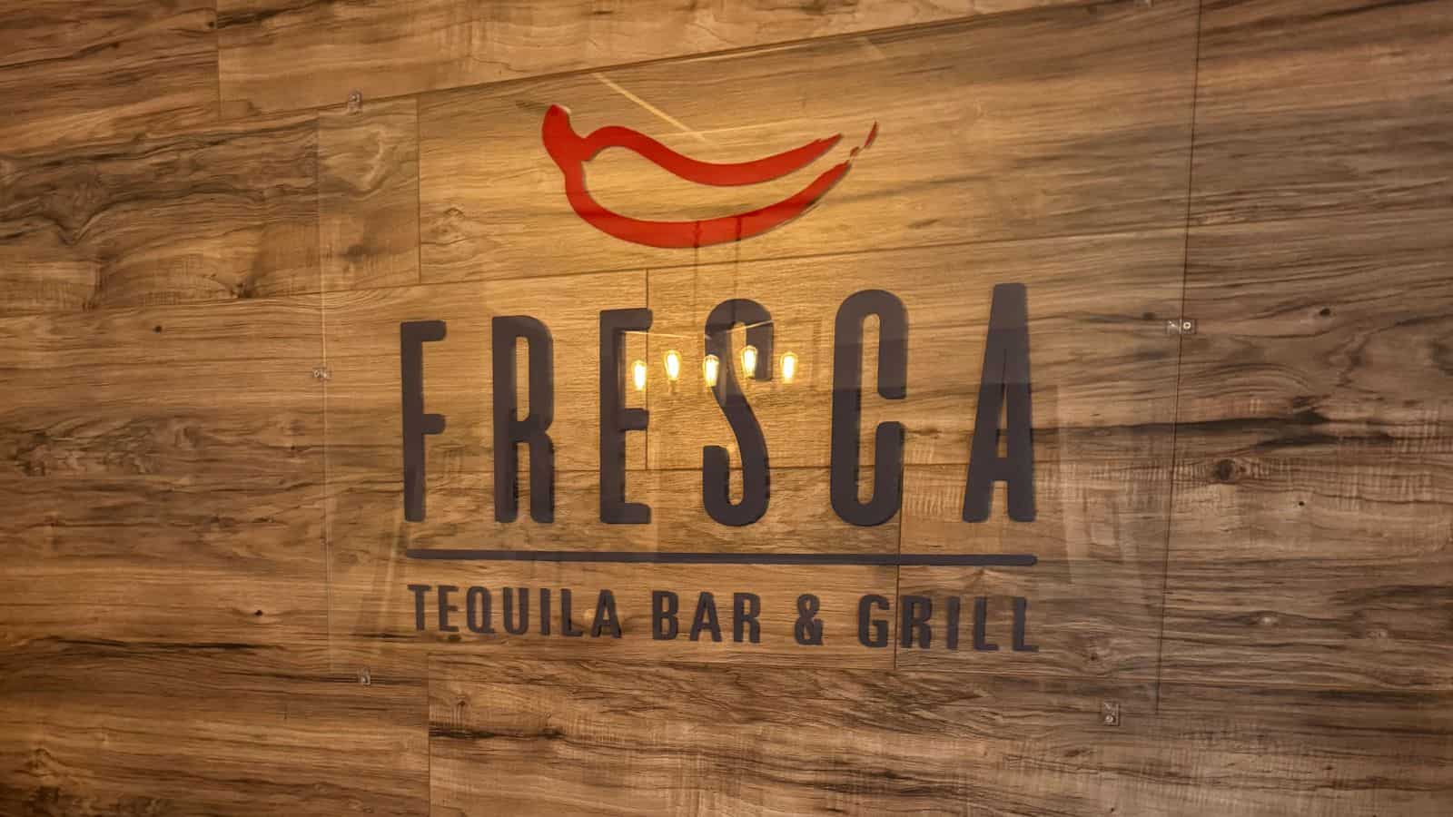 Sign reading “Fresca Tequila Bar & Grill” with a red chili pepper logo, mounted on a wood-paneled wall.
