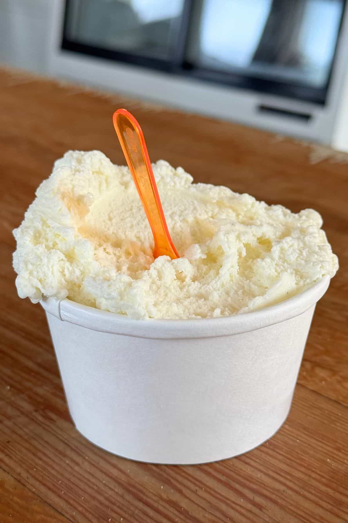 A cup of vanilla ice cream with an orange plastic spoon, placed on a wooden surface, evokes the simple joys of summer afternoons on Monhegan Island.