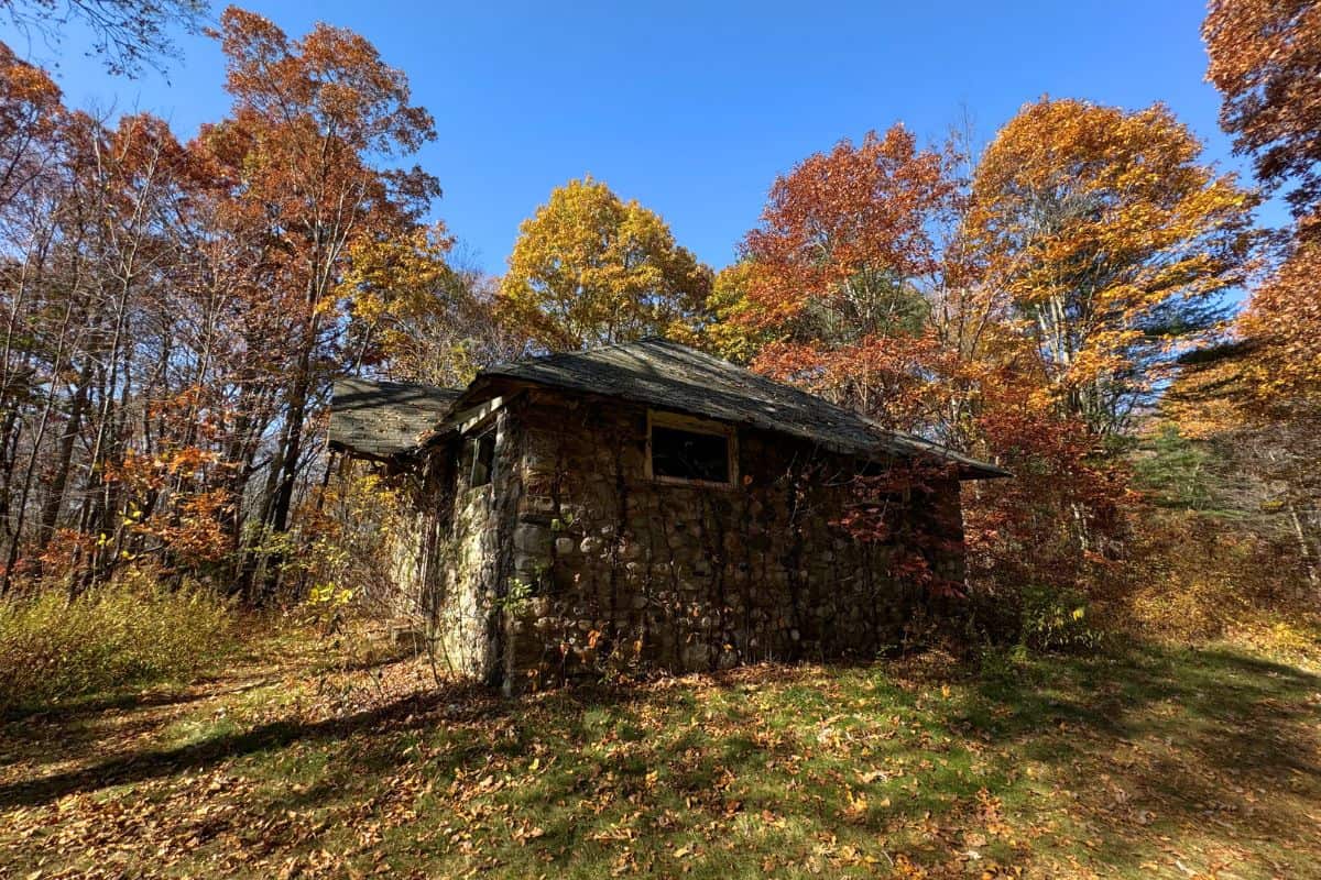 A small, abandoned stone building surrounded by colorful autumn trees under a clear blue sky.