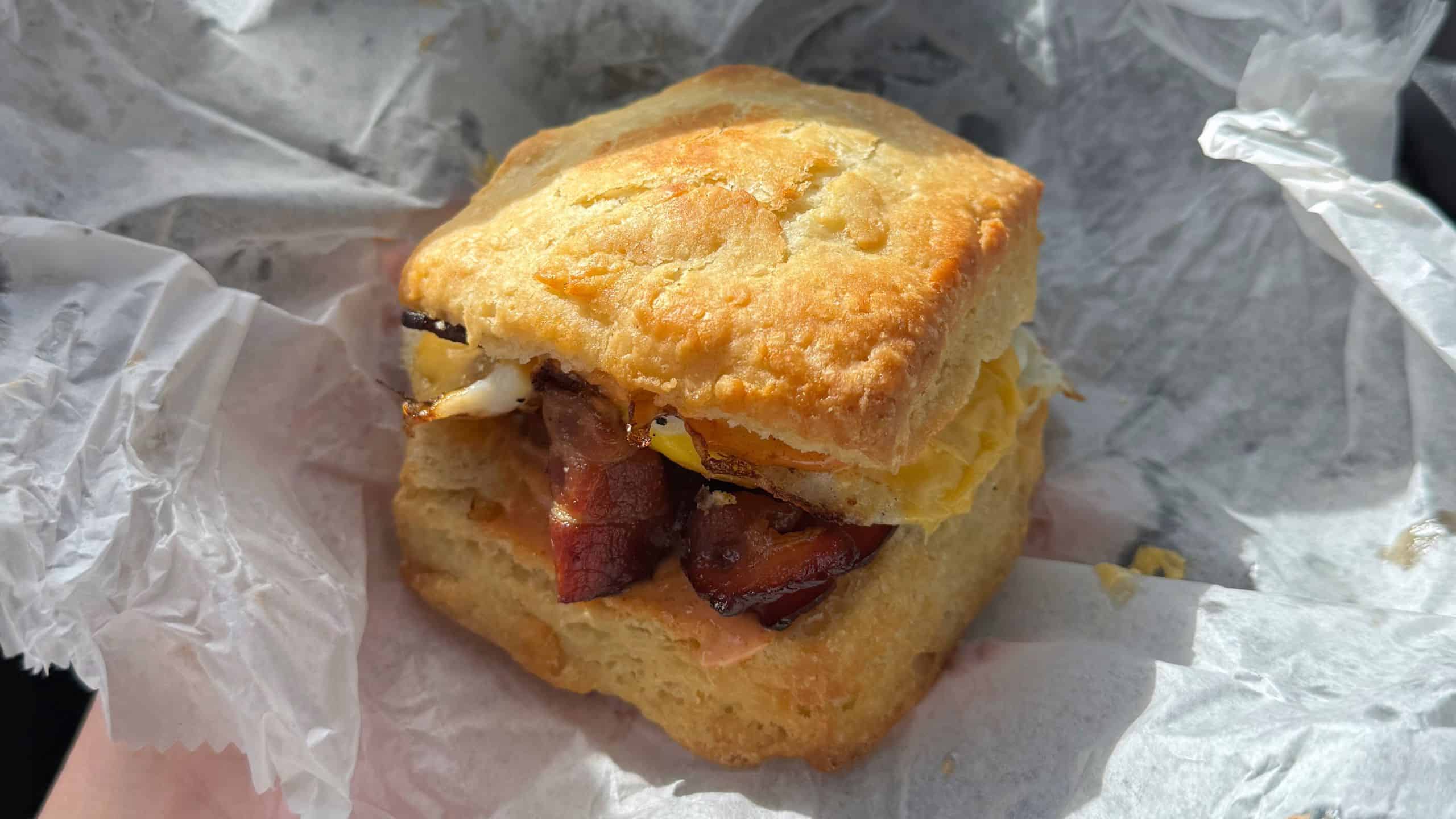 A biscuit sandwich with bacon and egg on white parchment paper, just like those served at the best breakfast places in Connecticut.