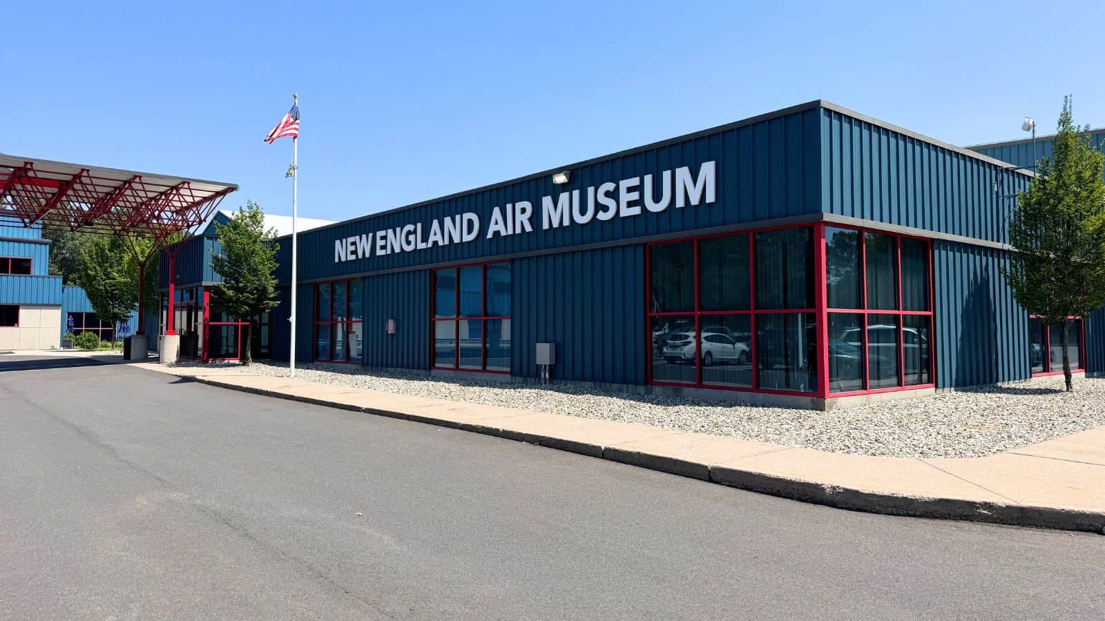 Exterior view of the New England Air Museum building with blue walls, red trim, an American flag, and clear sky.