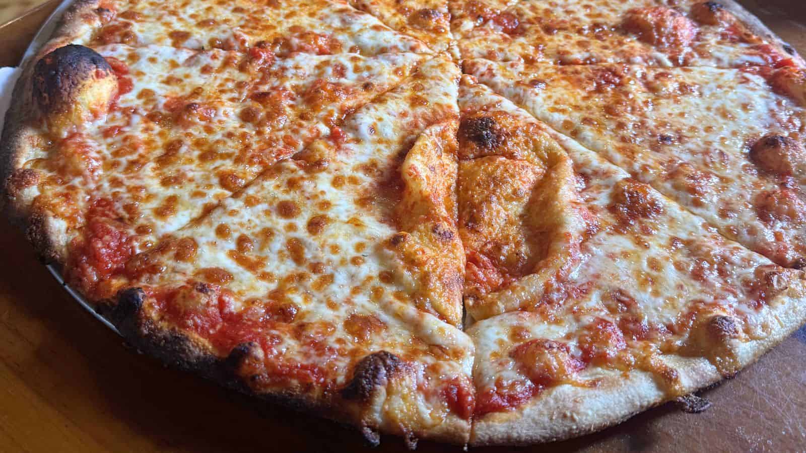 A cheese pizza with one slice showing a large area of sauce without cheese, served on a metal tray on a wooden table.