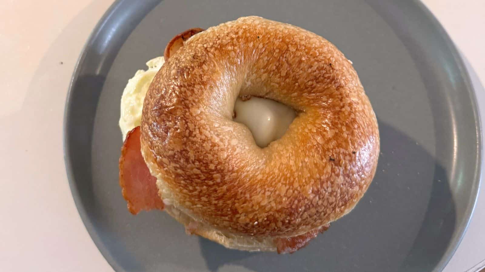 A sesame seed bagel sandwich with bacon and egg, served on a grey plate.