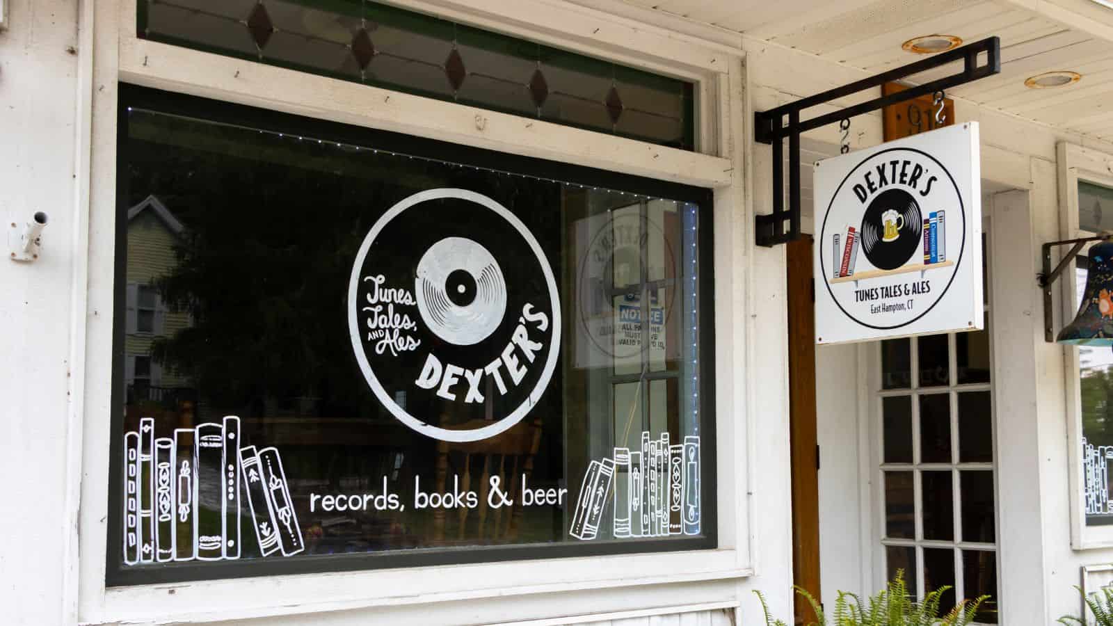 The storefront of Dexter’s features a large window with illustrations of books and a record, advertising “records, books & beer,” and a hanging sign with similar branding.
