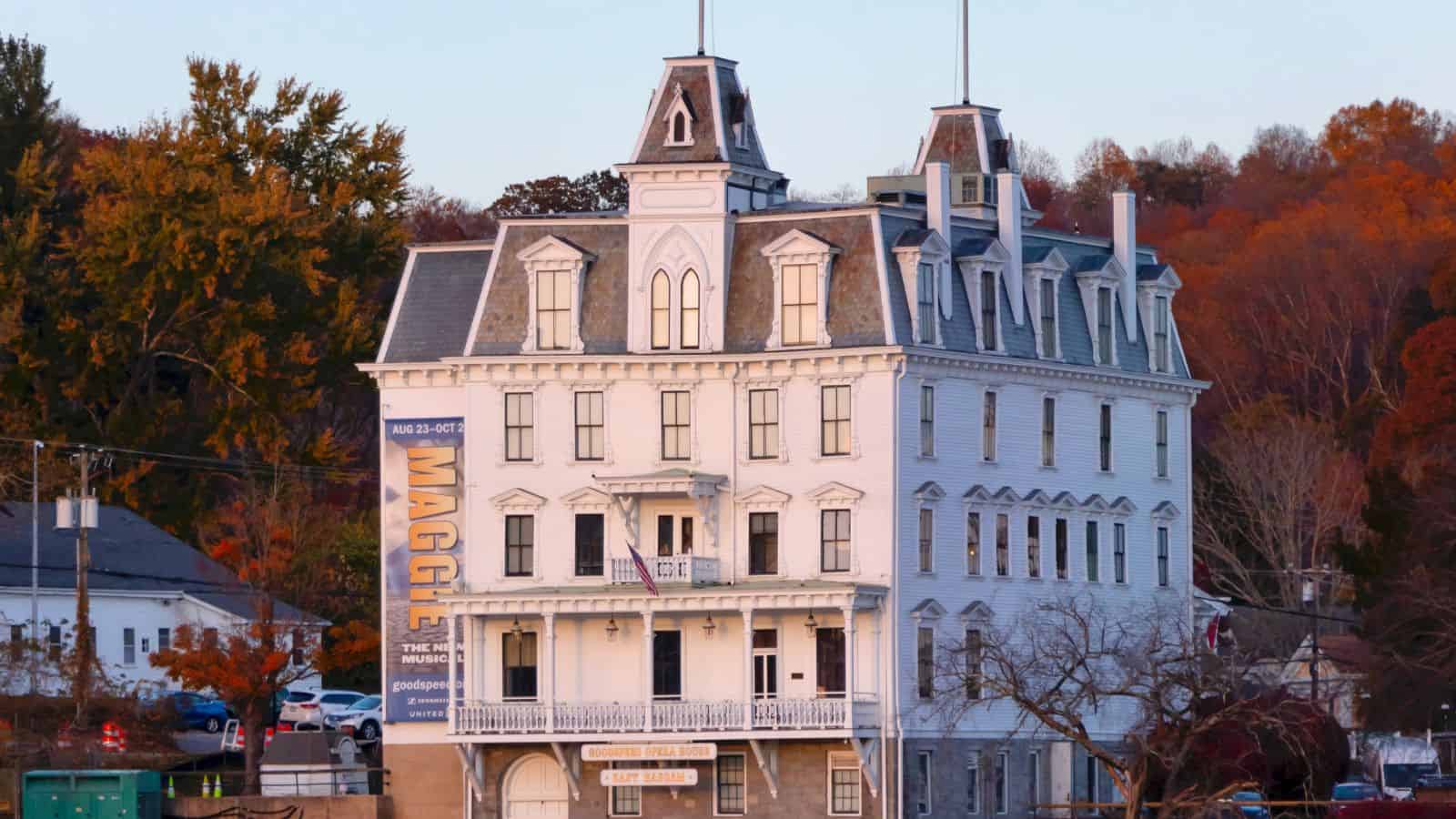 A large white historic building with a mansard roof, displaying a vertical "MAGEE" banner, surrounded by autumn trees.
