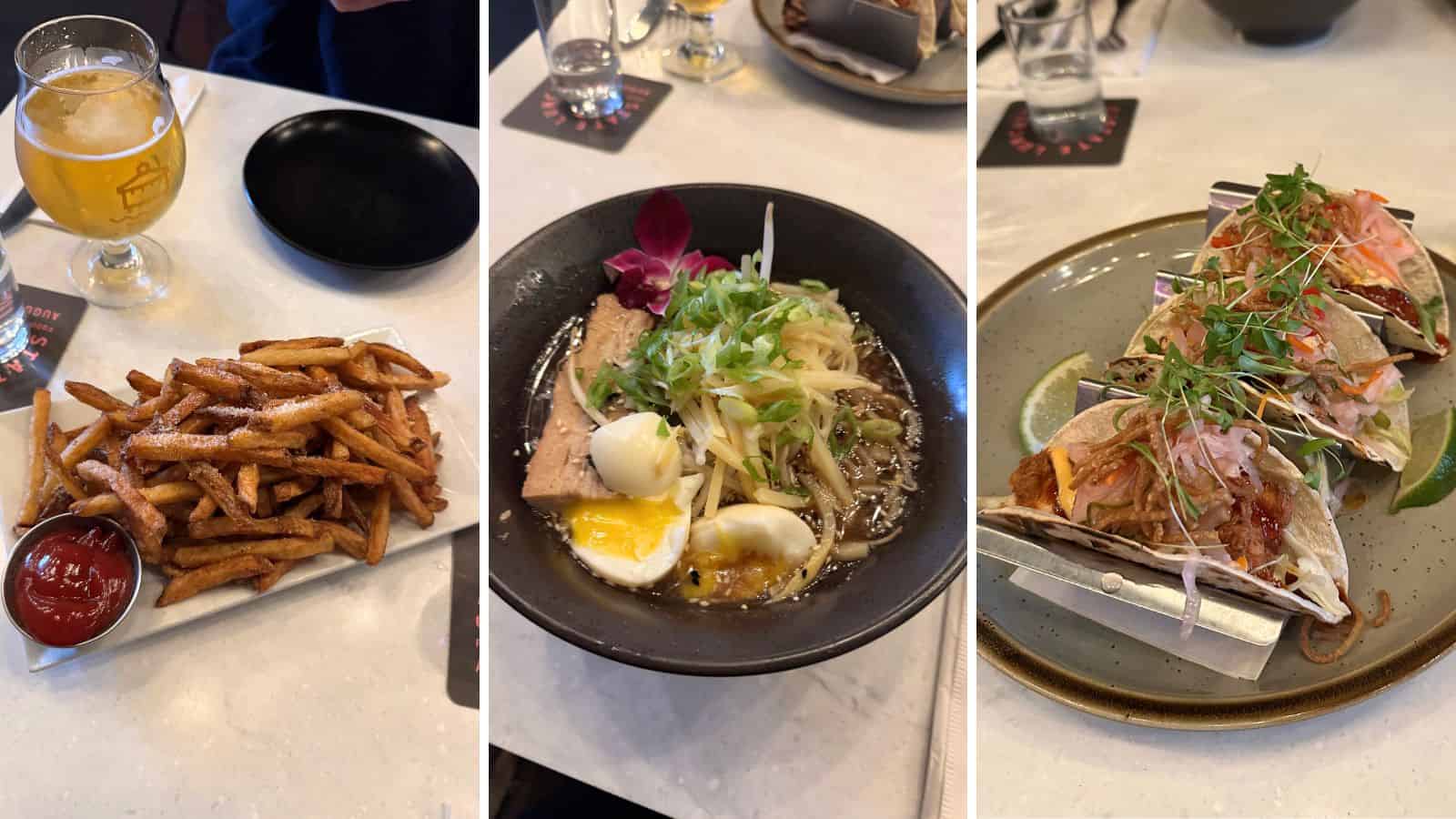 Three dishes on a table: a plate of French fries with ketchup, a bowl of ramen with egg and herbs, and a trio of tacos in a metal holder with garnish.