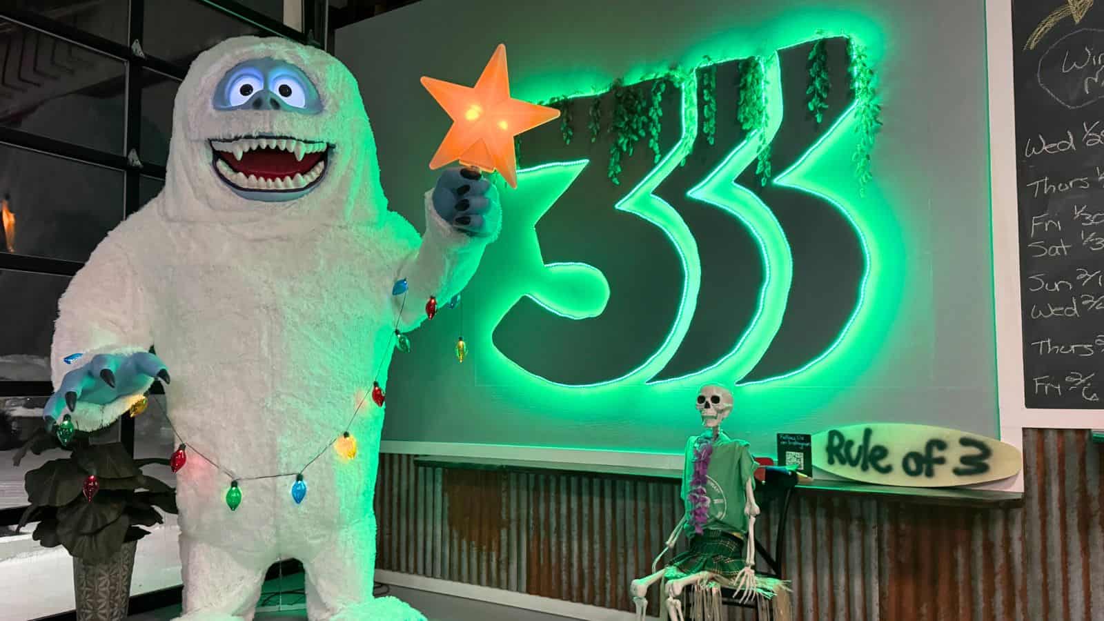 A large yeti figure with Christmas lights and a star stands next to a skeleton and a "Rule of 3" sign in front of a glowing green "333" wall display in East Hampton, Connecticut.