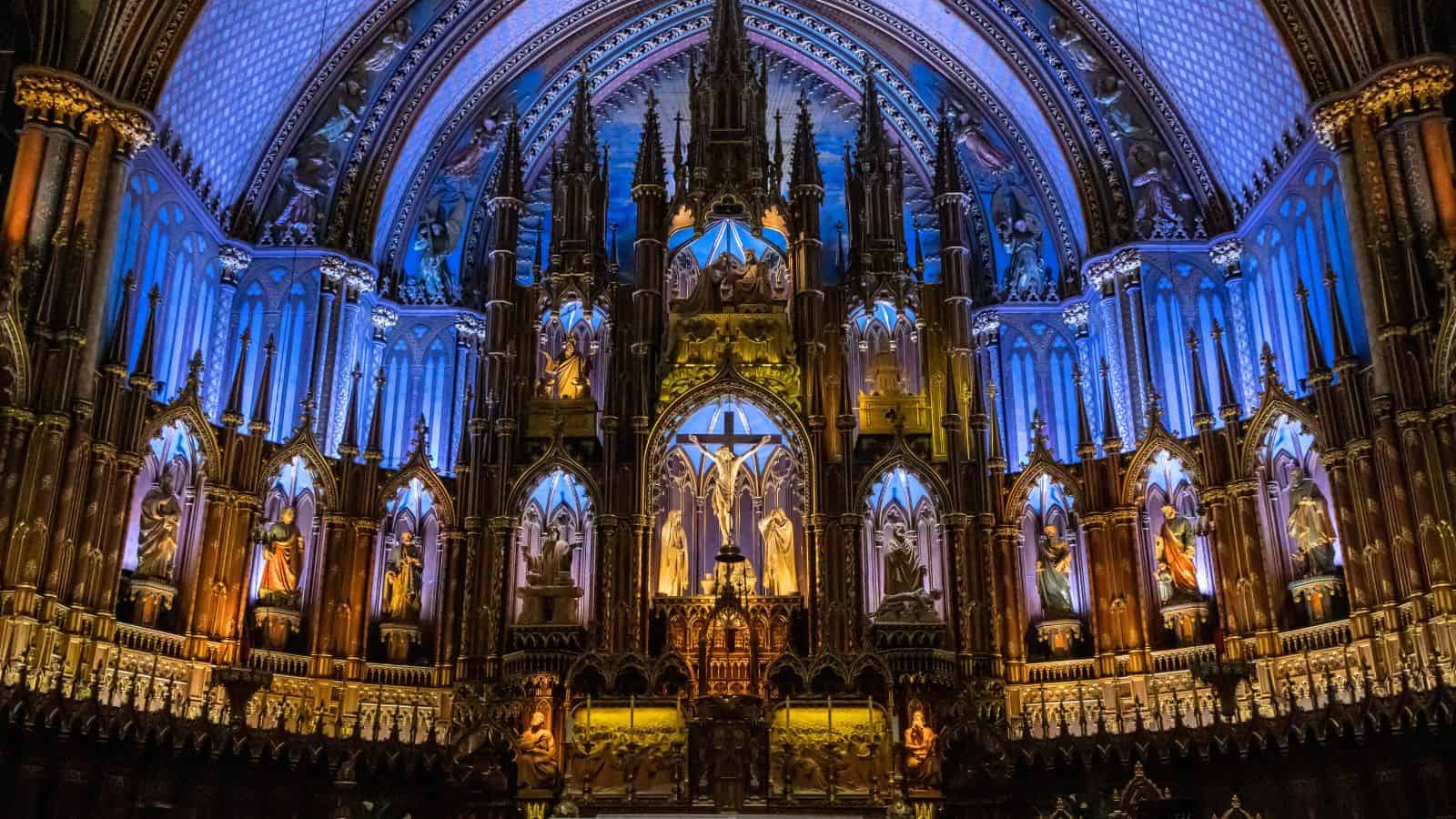 Ornate church altar with intricate carvings, statues, and bright blue and gold lighting highlighting architectural details.