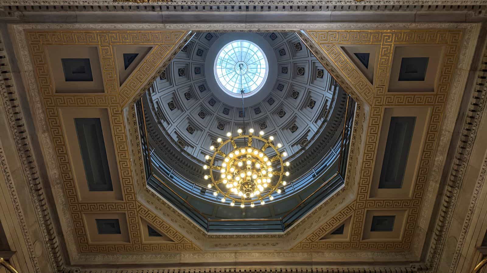 View of an ornate domed ceiling with a central chandelier and geometric architectural details, seen from directly below.