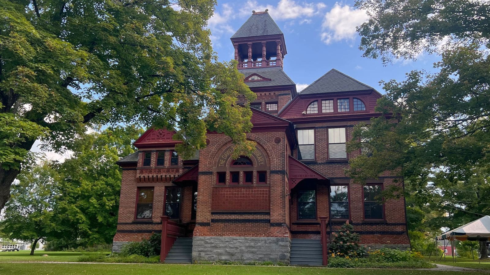A large, historic brick building with a central tower and arched entrance, surrounded by trees and greenery under a partly cloudy sky—reminiscent of the charm found in historic Connecticut towns.