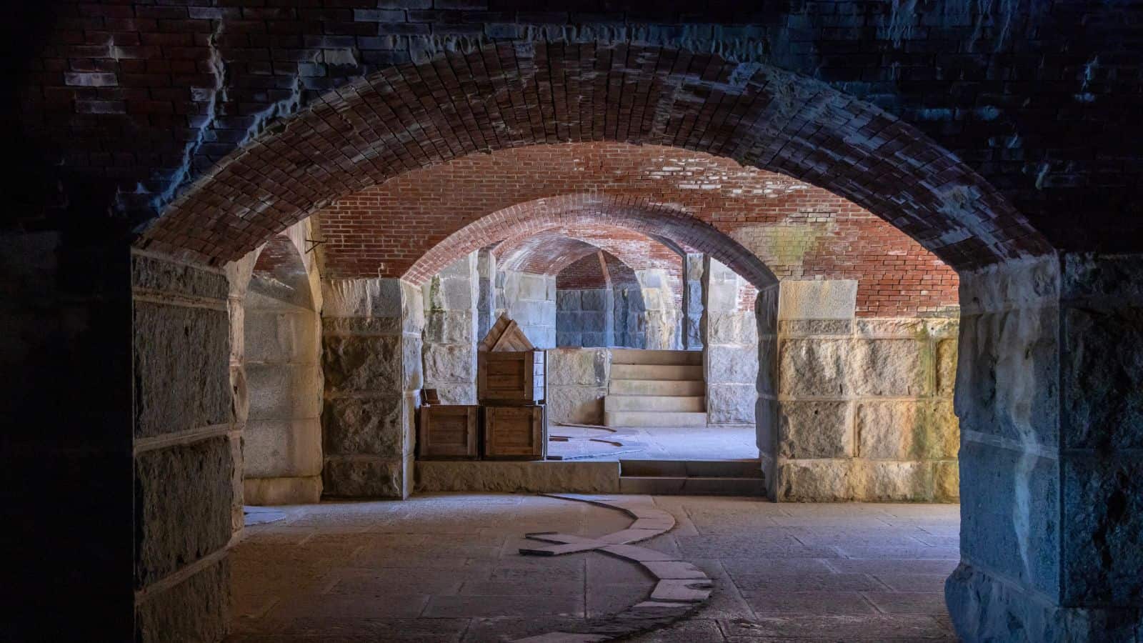 Interior view of an old stone and brick fort with arched ceilings, thick walls, and wooden crates placed on the floor—one of many haunted places around New England known for its mysterious atmosphere.
