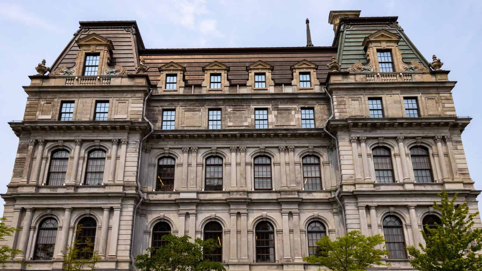 Stone facade of a historic, multi-story building with arched windows and a mansard roof—one of the architectural gems you’ll discover while exploring things to do in Montreal.