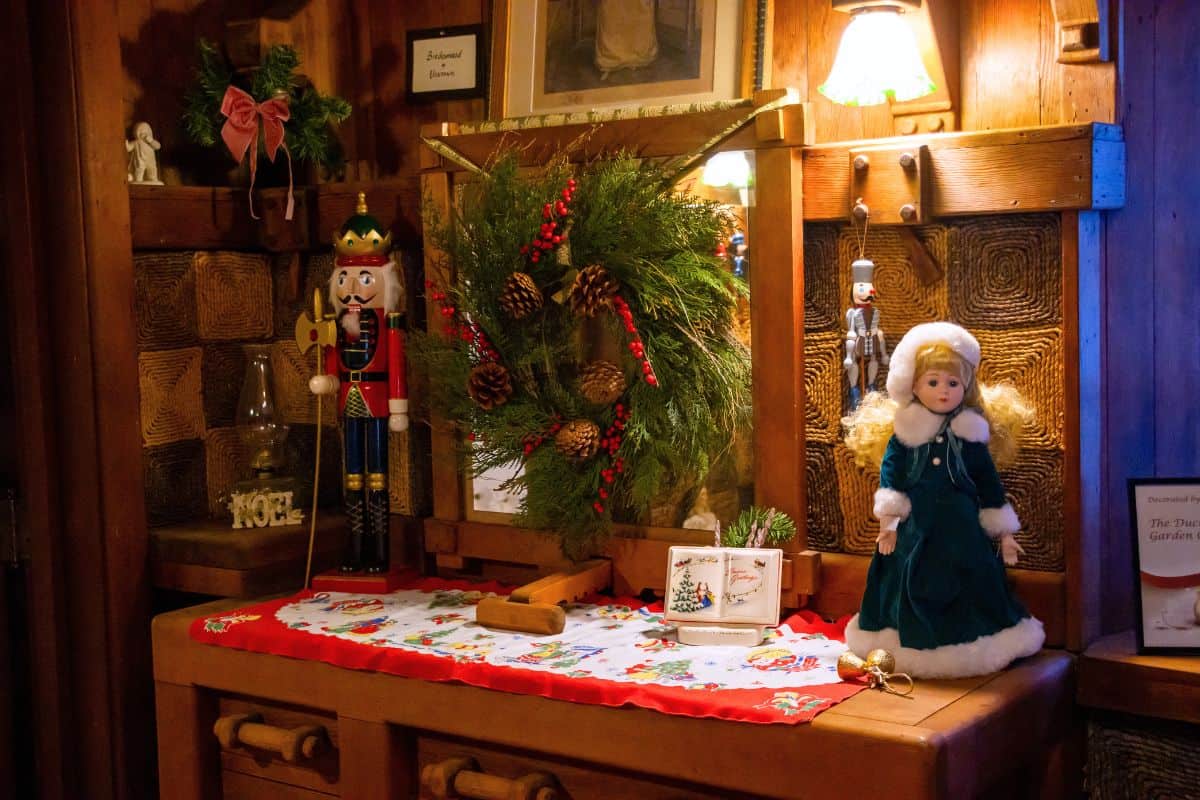 A wooden cabinet decorated with a nutcracker, a winter doll, a pine wreath, holiday cards, and a lamp, creating a festive Christmas scene.