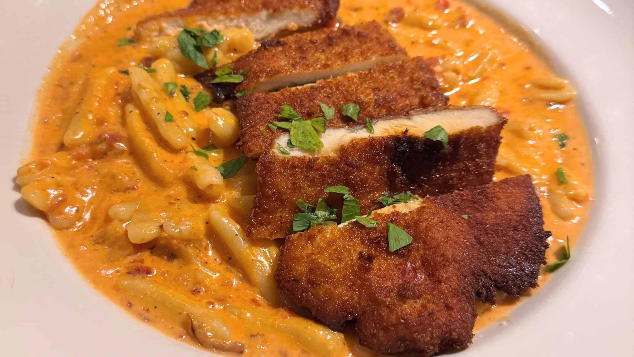 Pasta in a creamy orange sauce topped with sliced breaded and fried chicken, garnished with chopped parsley.