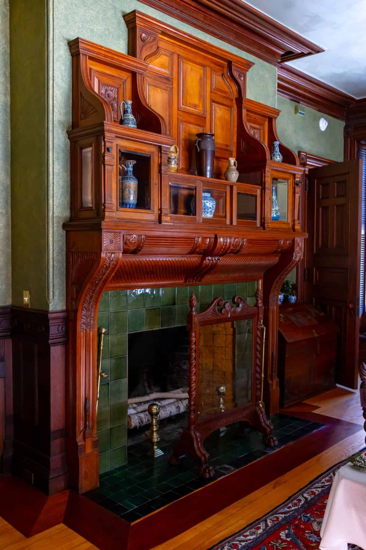 Ornate wooden fireplace with green tile surround, decorative shelving, and various ceramic vases displayed on the mantel.
