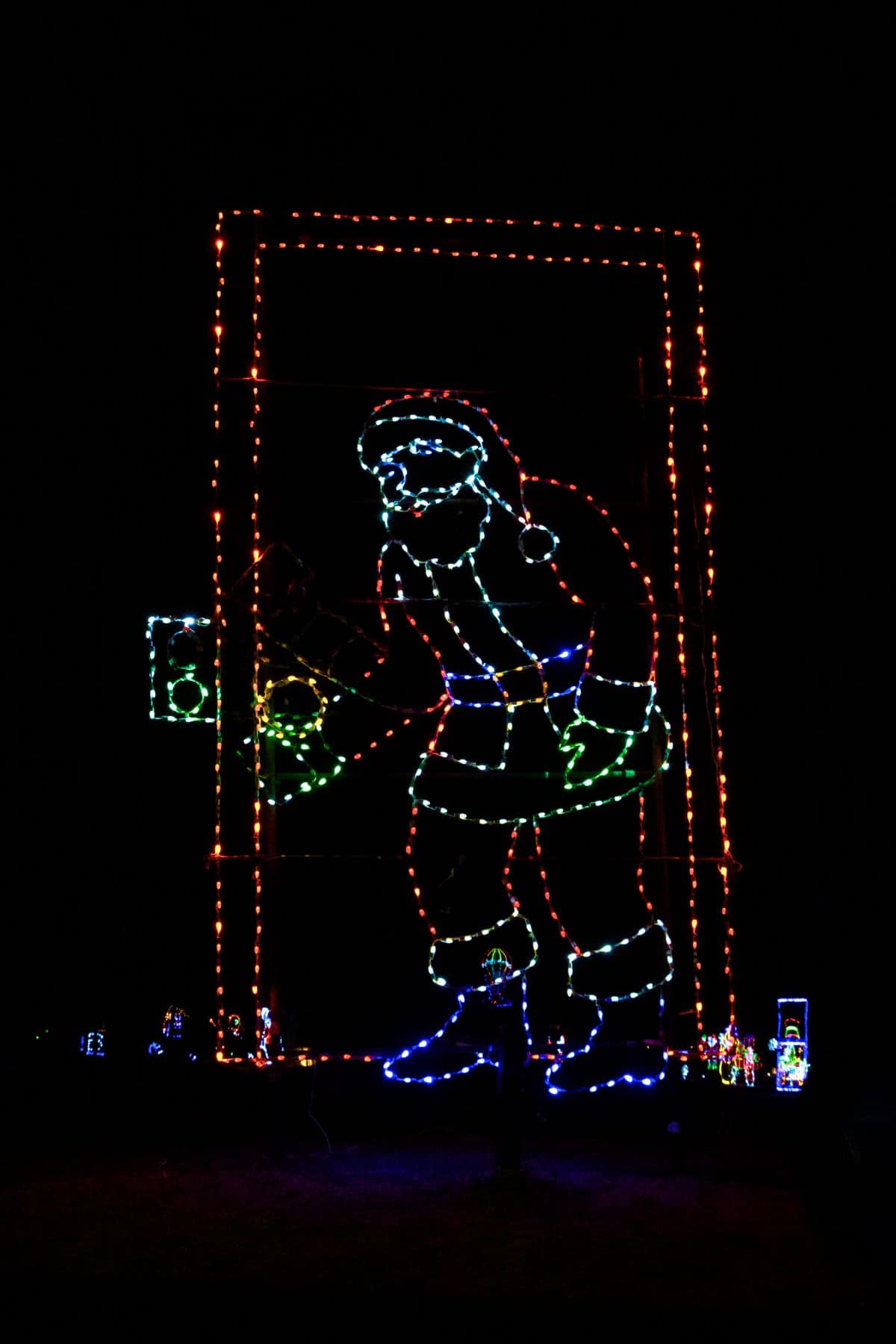 Outline of Santa Claus made from colorful holiday lights, holding a small object and framed by a rectangular border, displayed against a dark background.
