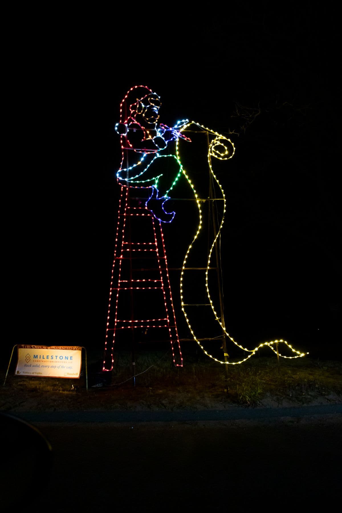A holiday light display at Fantasy of Lights CT features Santa Claus on a ladder reading a long list, with a sign for Milestone Companies beside him.