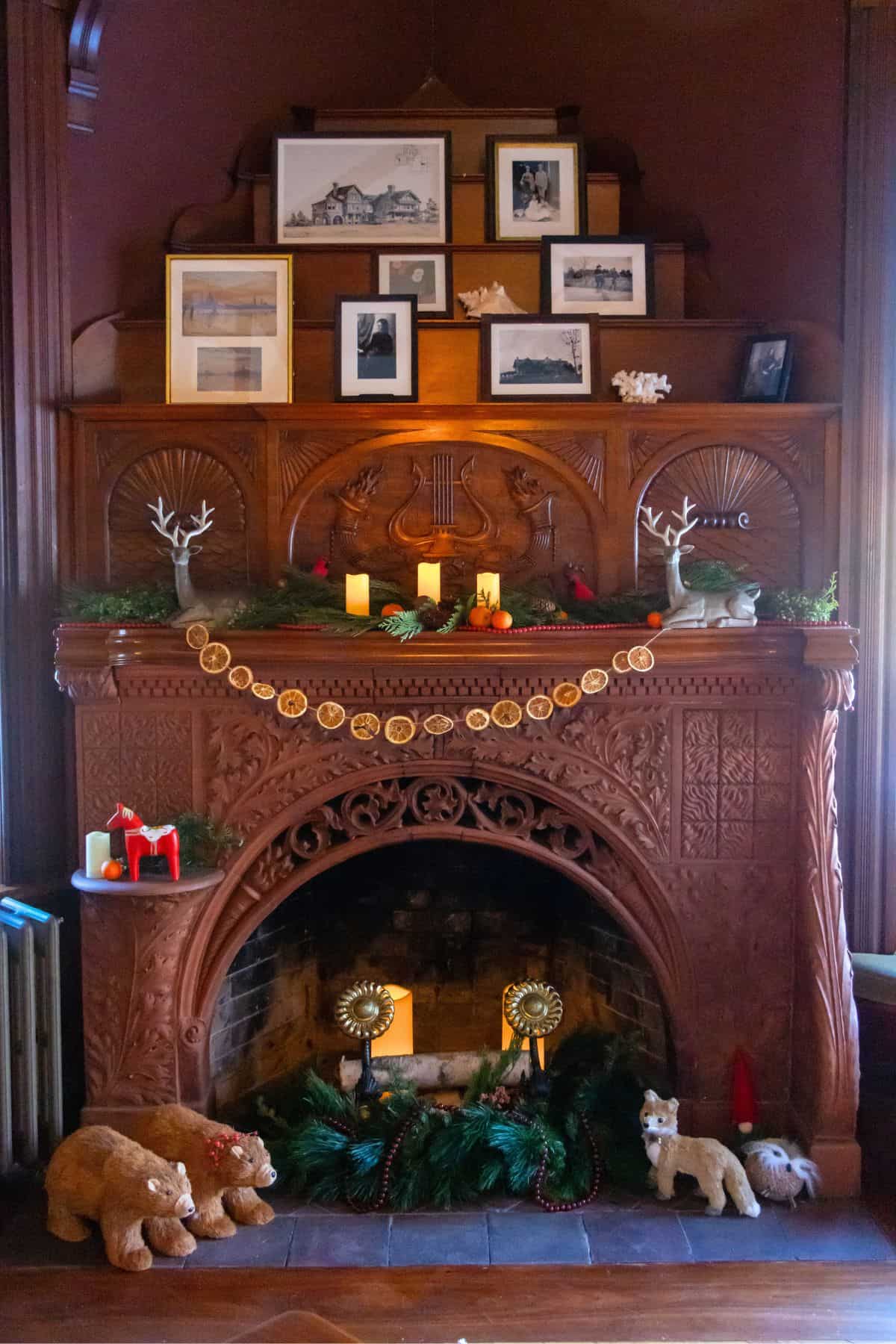 A decorated wooden fireplace featuring framed photos, faux candles, garlands, toy animals, and holiday ornaments arranged on the mantel and hearth.