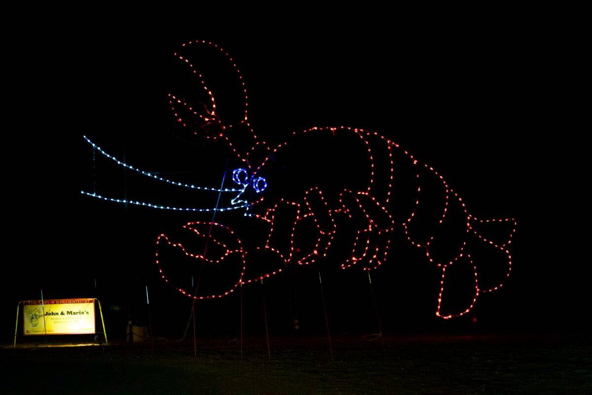 A lobster outline made of red and blue lights is displayed at night, with a small illuminated sign visible in the lower left corner.