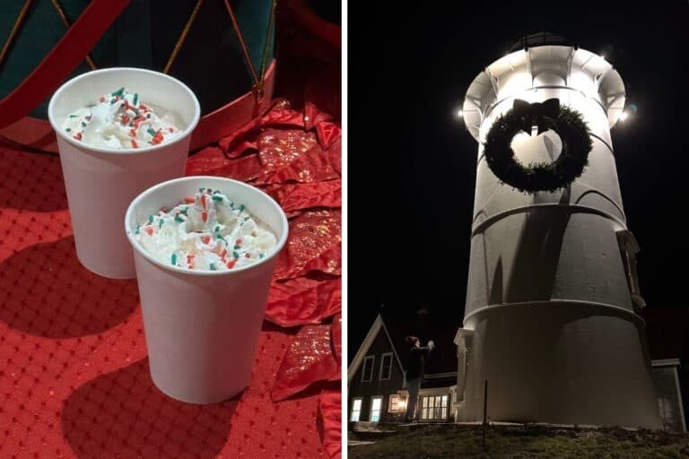 Two cups of hot chocolate with whipped cream and sprinkles on a red surface; next to a white lighthouse decorated with a holiday wreath at night.