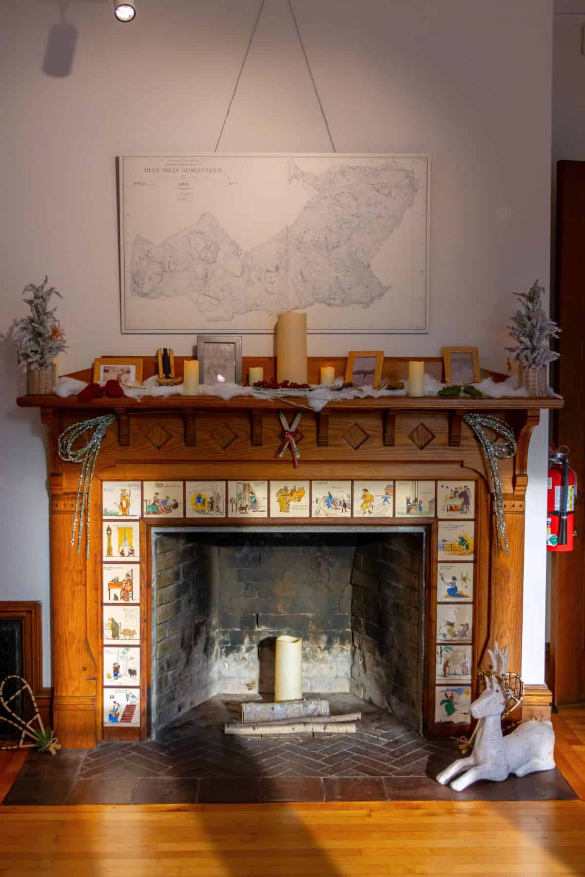 A wooden fireplace decorated with candles, framed photos, garlands, and two decorative deer, with a map hanging above the mantel.